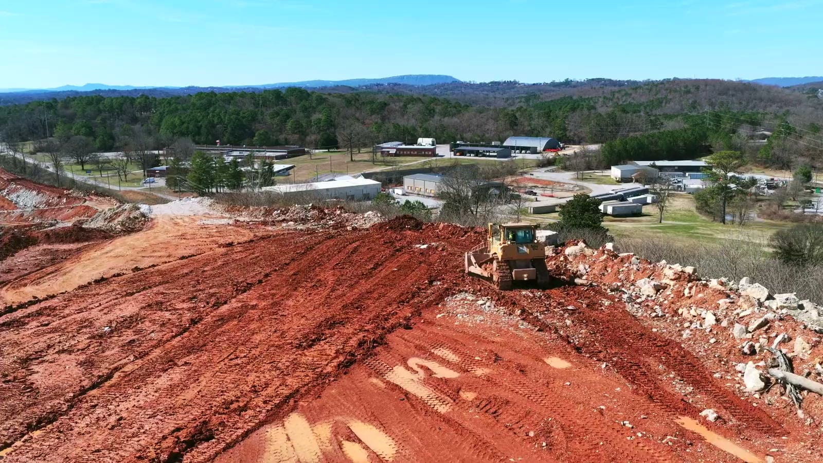 Aerial view of a dozer clearing red-earth land with a town and hills behind