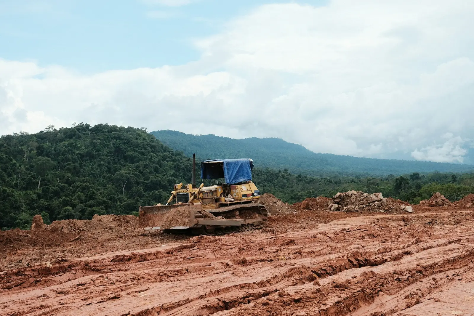 A dozer on freshly cleared red earth with forested mountains behind it
